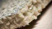 Close-up comparison of mineral wool and fiberglass insulation rolls on wooden floor in well-lit room.
